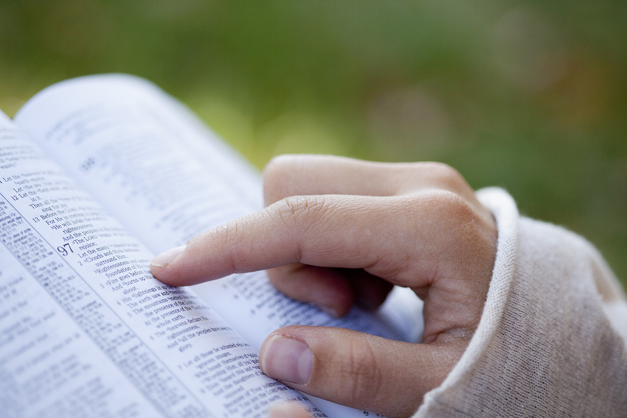 Close-up of woman's hands while reading the Bible outside.